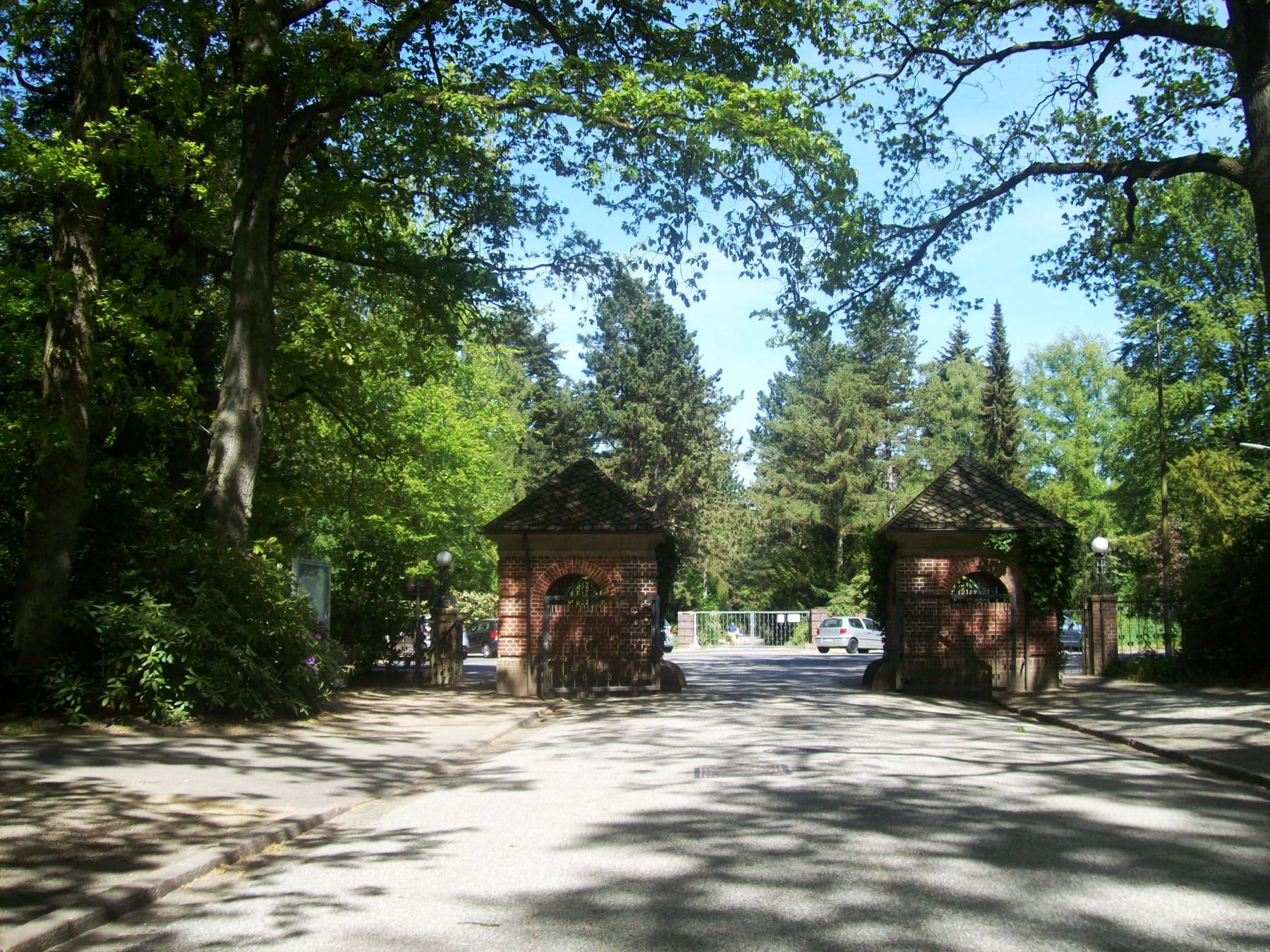 Offene Toranlage aus rotem Backstein am Ende einer baumbeschatteten Zufahrt auf Friedhof Bergedorf