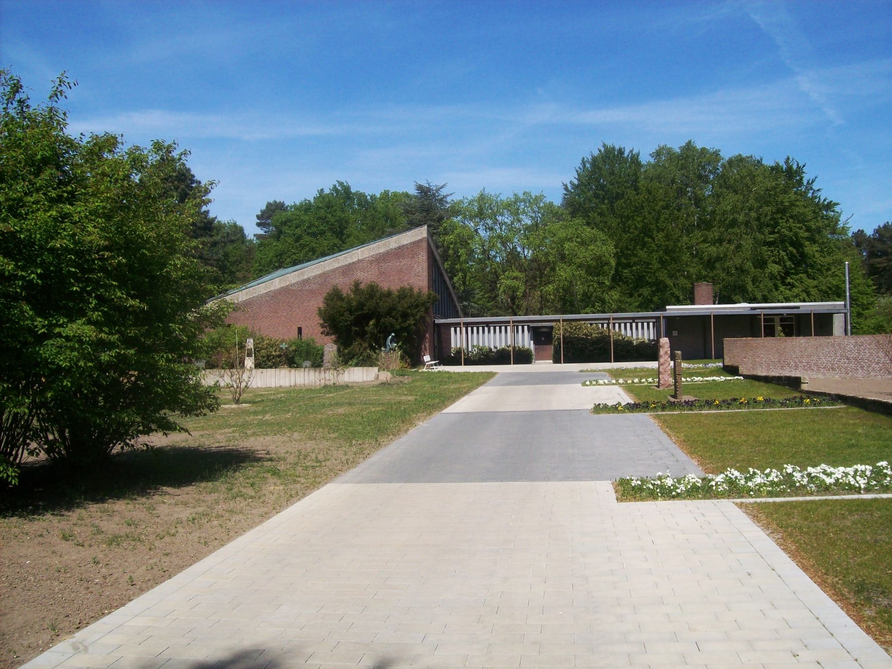 Ein gerader Weg führt über die Friedhofsanlage zur niedrigen, modernen Kapelle II aus rotem Backstein; seitlich liegen kleine Grabfelder und Gehölze. auf Friedhof Bergedorf